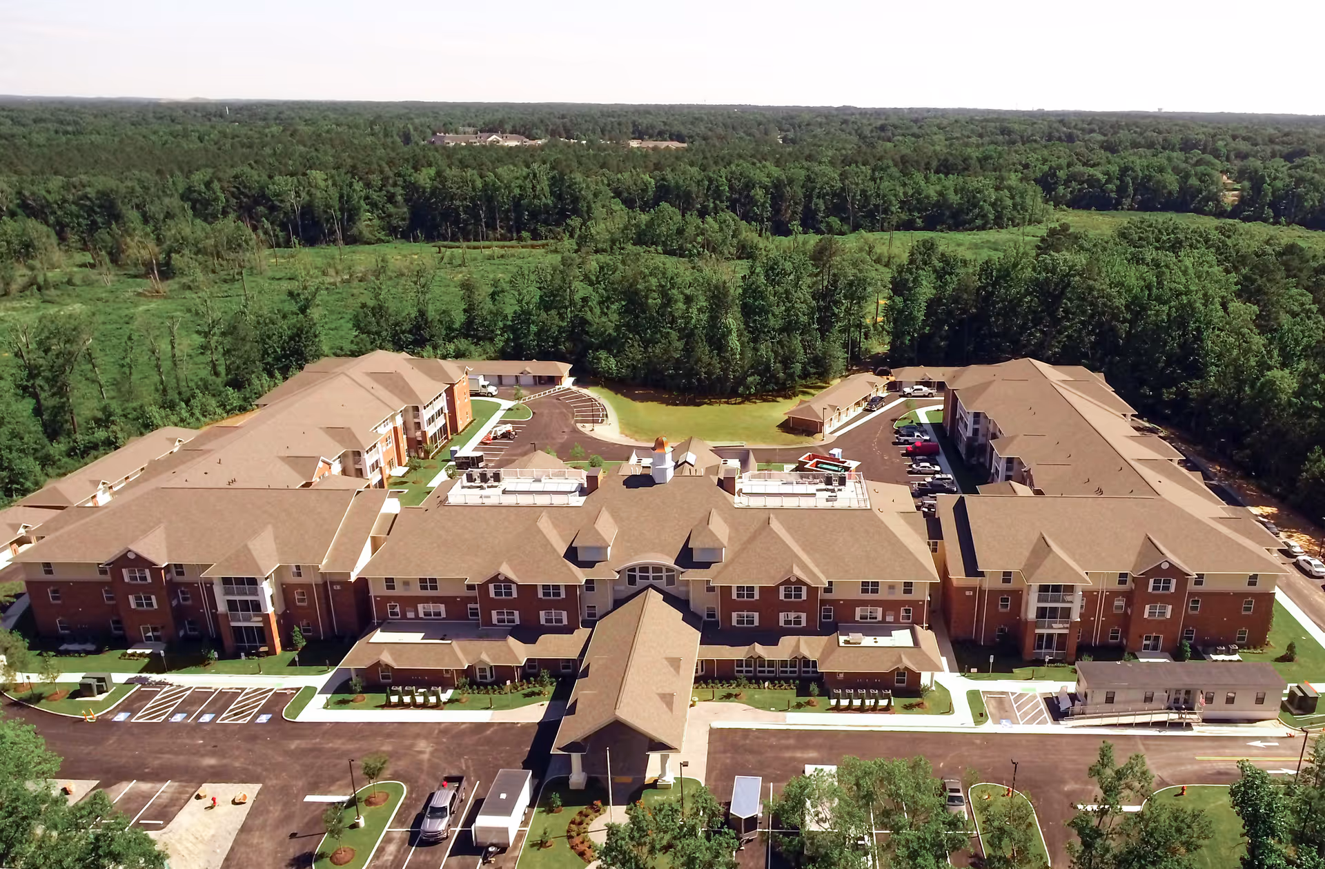 Aerial view of a large brick retirement community with multiple connected buildings and surrounding trees.