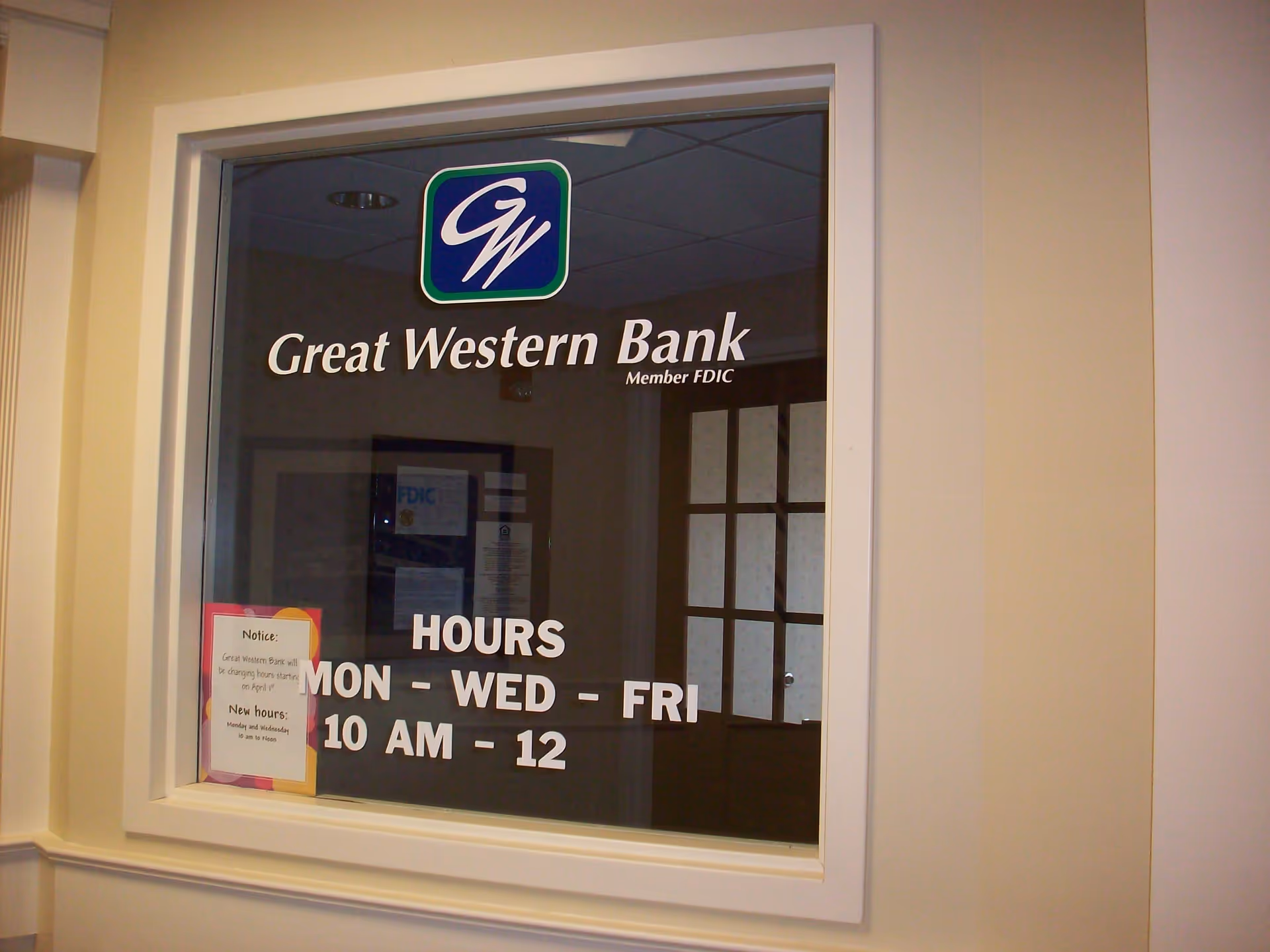 Window with signage for Great Western Bank, displaying the logo and hours of operation as Monday, Wednesday, and Friday from 10 AM to 12 PM. There is a notice about changing hours starting April 1st posted on the window.