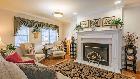 Cozy living room with sofa and armchairs arranged around a decorative fireplace and patterned area rug.