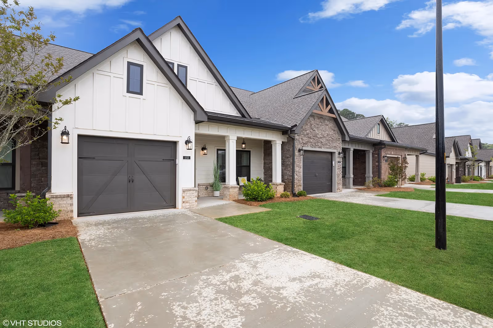 Exterior view of a row of modern single-story homes with garages, driveways, and well-maintained lawns under a blue sky with some clouds.