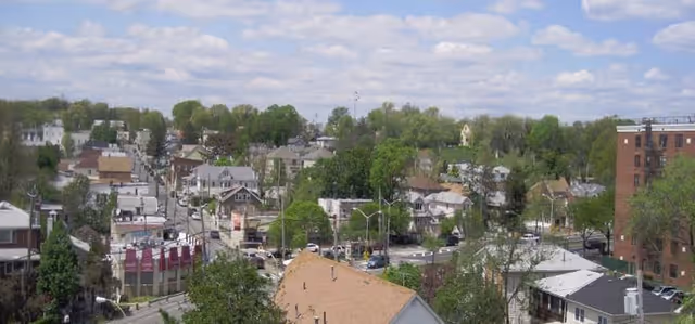 Aerial view of a suburban neighborhood with houses, trees, and streets under a partly cloudy sky.