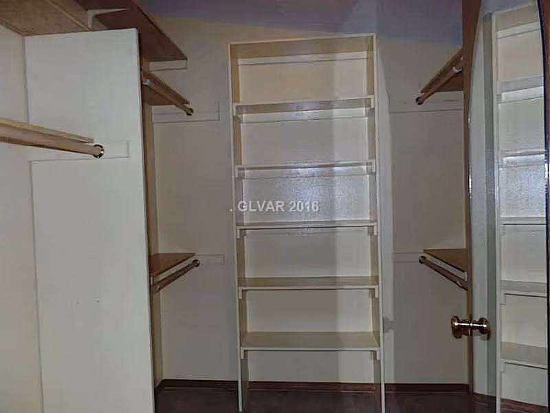 Empty walk-in closet with built-in shelves, multiple hanging rods, and a mirrored door.