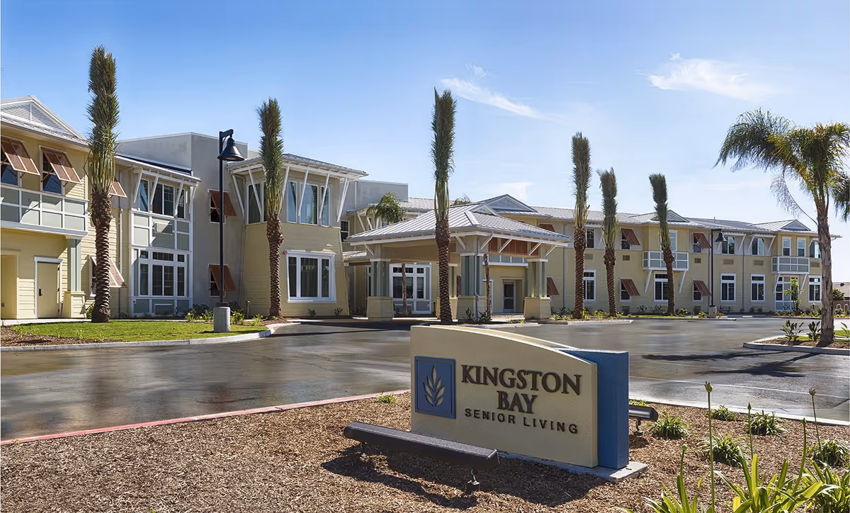 Exterior view of Kingston Bay Senior Living building with palm trees and a front sign.