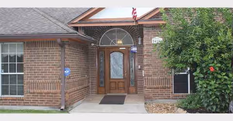 Brick building front entrance with arched window, wooden door, and flag.