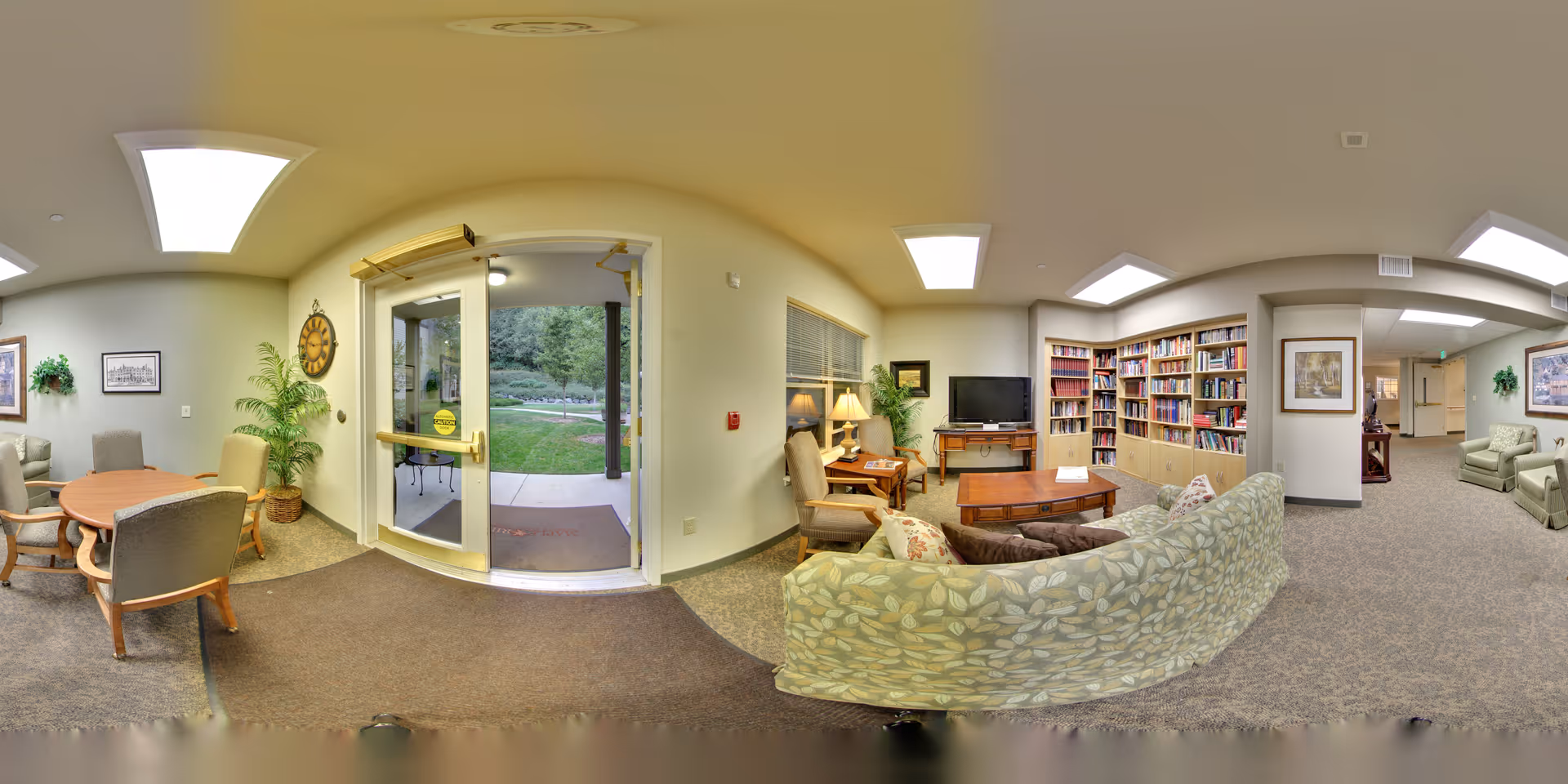 Cozy communal lounge and entry area with a curved patterned sofa, bookshelves, seating and a glass door leading outside.
