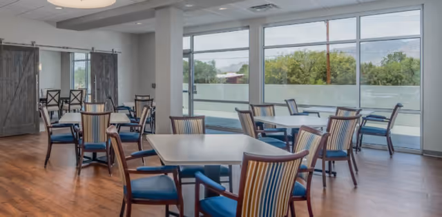 Bright dining area with multiple tables and striped-upholstered chairs facing large windows overlooking trees and distant hills.
