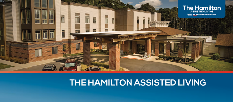 Front exterior of The Hamilton Assisted Living building with a covered entrance and parked cars.