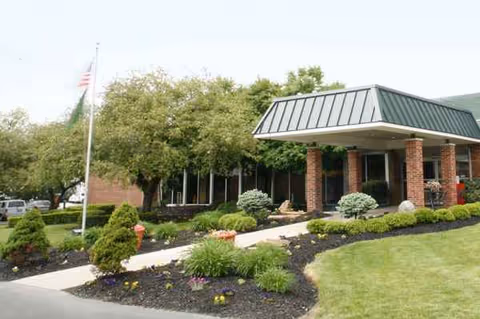 Senior living facility front entrance with brick columns, glass windows, and manicured landscaping.