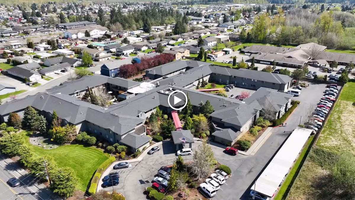 Aerial view of a large retirement and assisted living complex with connected buildings, parking lots, landscaped lawns, and surrounding neighborhood.