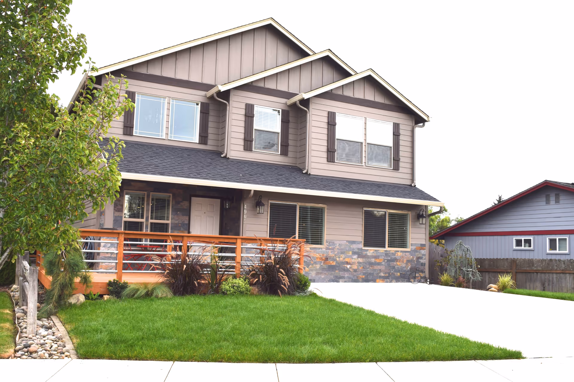 Two-story suburban house with a covered front porch, green lawn, and a driveway.
