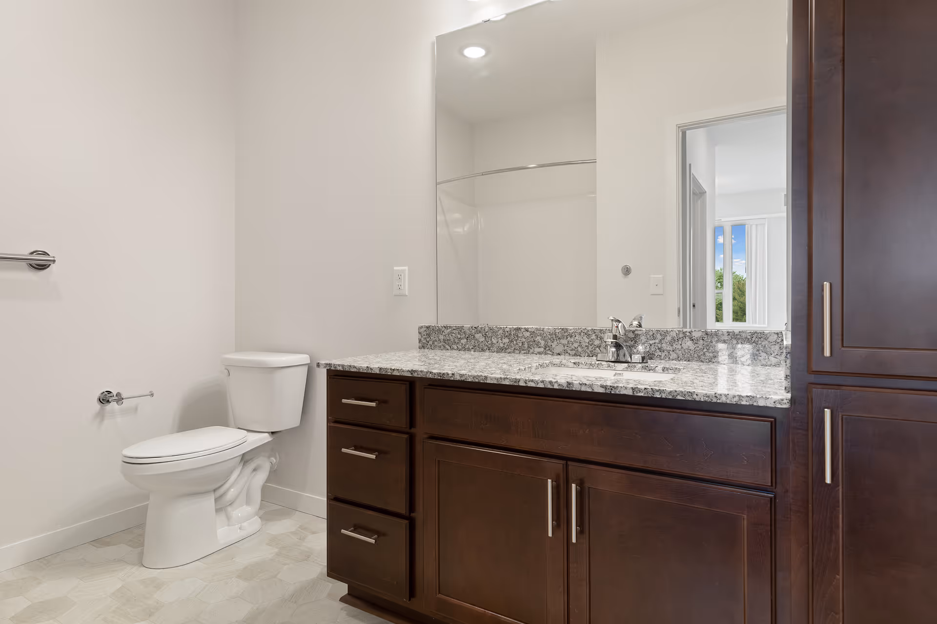 Bathroom with a toilet, granite-topped vanity and sink, dark wood cabinets, and a large mirror.