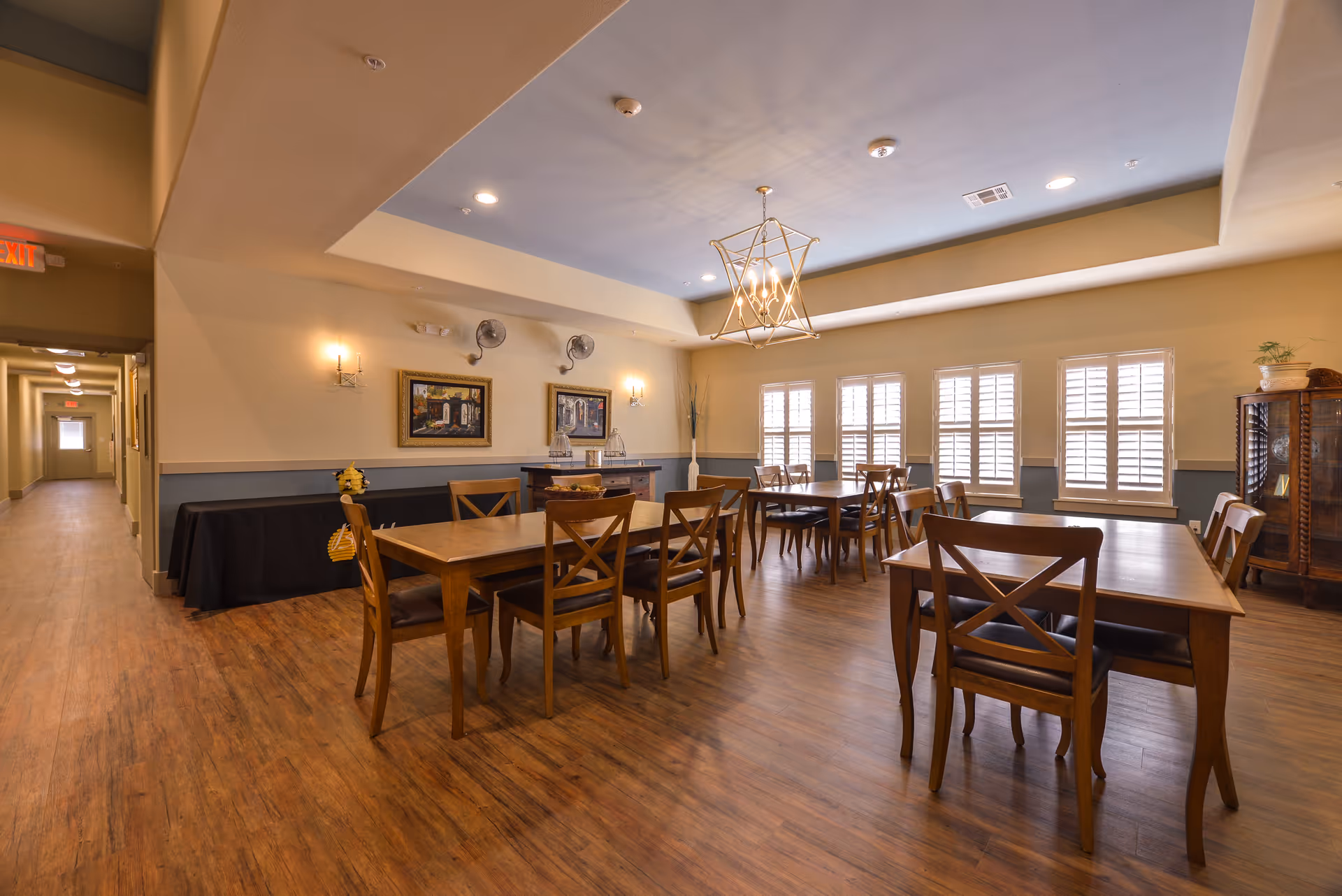A spacious dining room with wooden tables and chairs, hardwood floors, and sunlit windows.