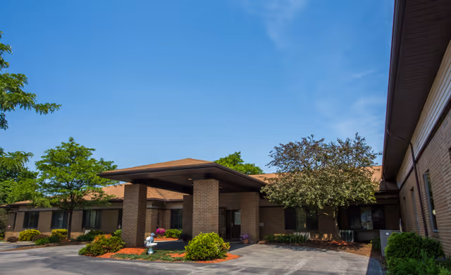 Exterior view of Grove Manor with a covered entrance, brick pillars, and manicured landscaping.