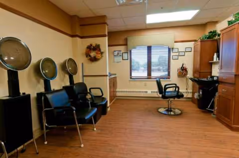Interior salon area with hair dryers, chairs, and a window at Oak Hills Living Center Assist.