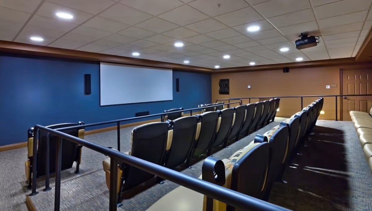 Small screening room with rows of theater seats facing a large projection screen and ceiling-mounted projector.