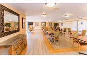 Spacious dining room with multiple tables and chairs, wood flooring, and a large mirror on the left wall.