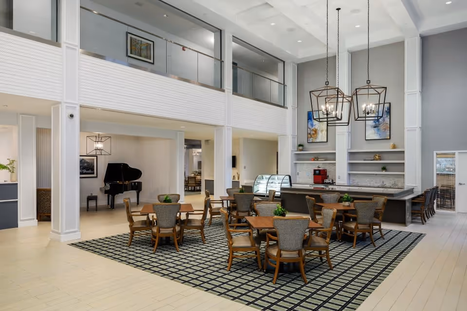 Spacious two-story communal dining area with multiple tables and chairs, a service counter, and a piano under high ceilings.