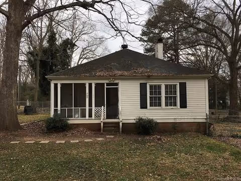 Small white single-story building with a screened front porch and leaf-covered yard.