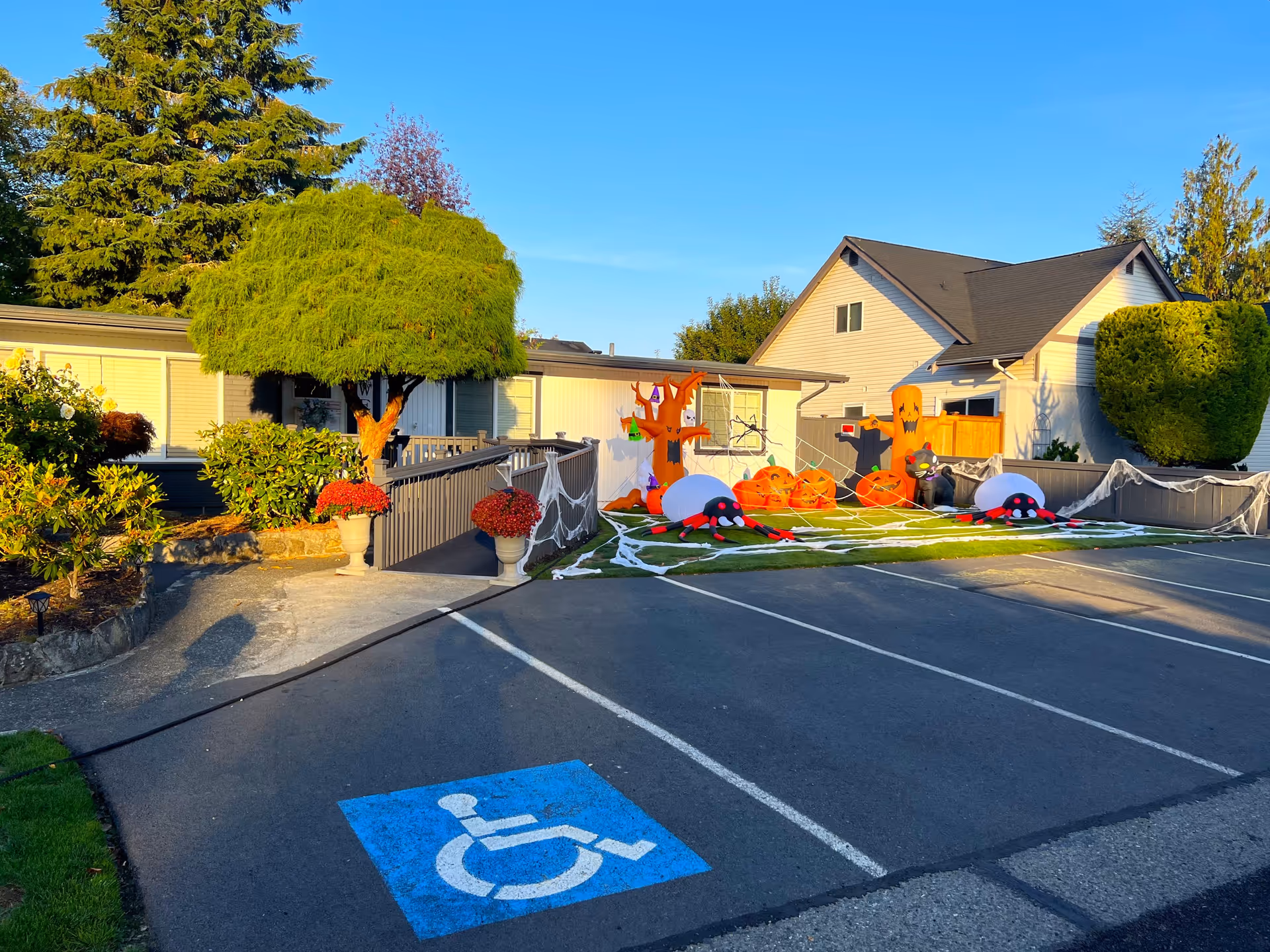 Front exterior of a senior care home with a parking lot, accessible parking space, and Halloween decorations on the lawn.