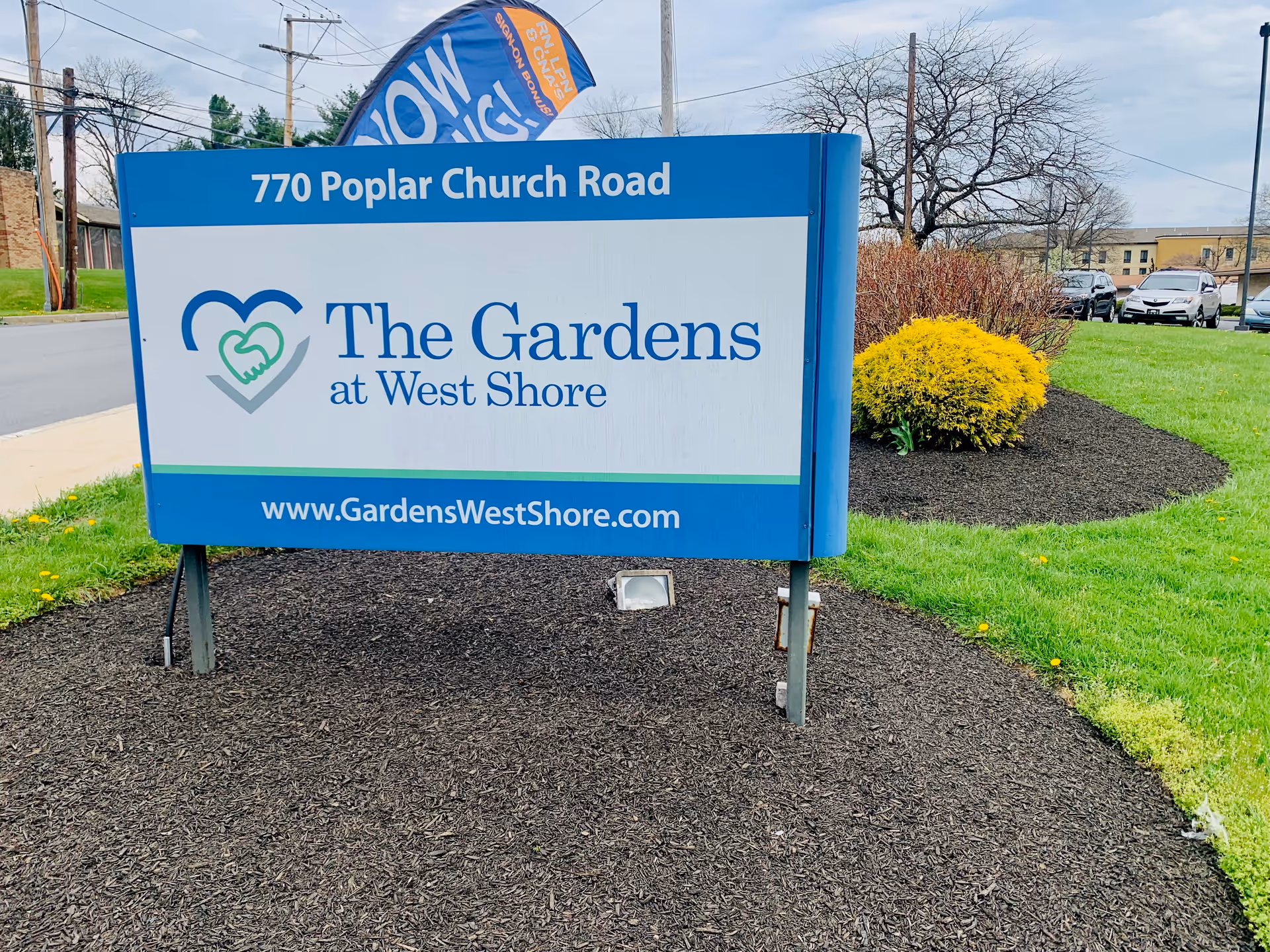 Outdoor landscaped sign reading 'The Gardens at West Shore' at 770 Poplar Church Road with website URL.
