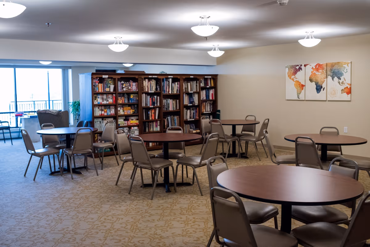 Communal activity room with round tables and chairs, bookshelves and a world-map artwork on the wall.