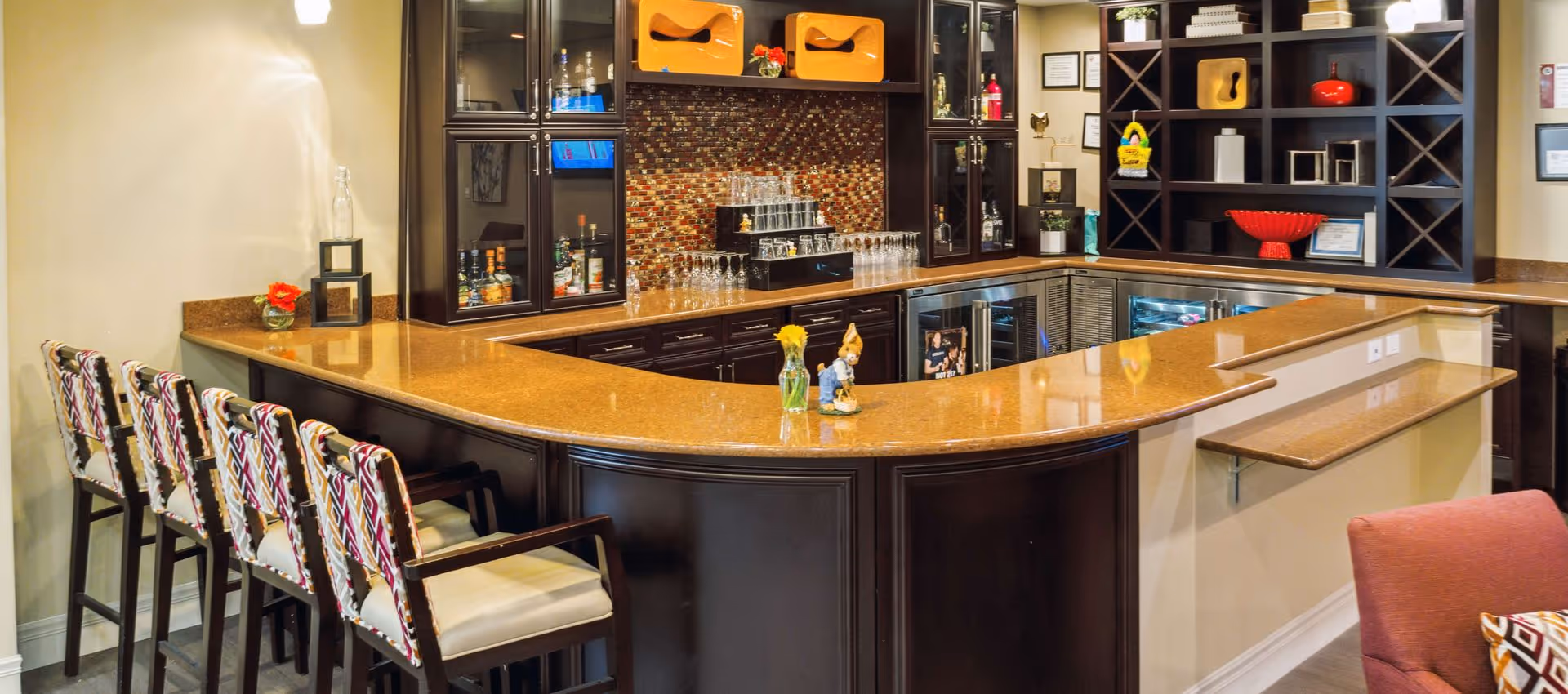 Curved countertop bar with patterned bar stools, shelving, and glassware in a communal lounge area.
