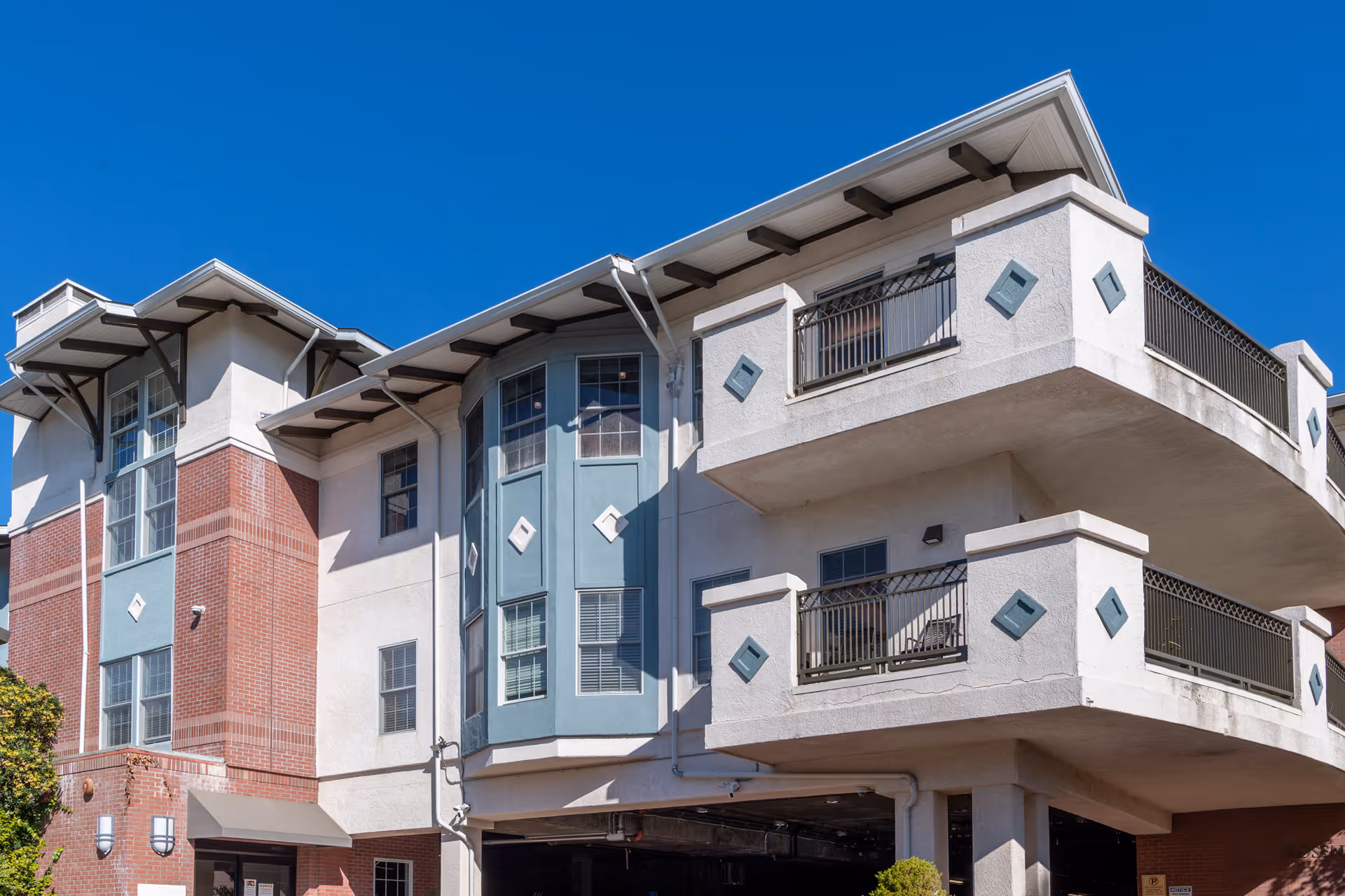 Front exterior of a multi-story senior living building showing balconies, bay windows, and a covered entry against a clear blue sky.