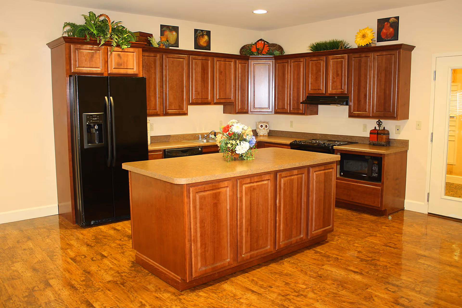 Bright kitchen with wooden cabinets, a central island topped with a floral centerpiece, and a black refrigerator.