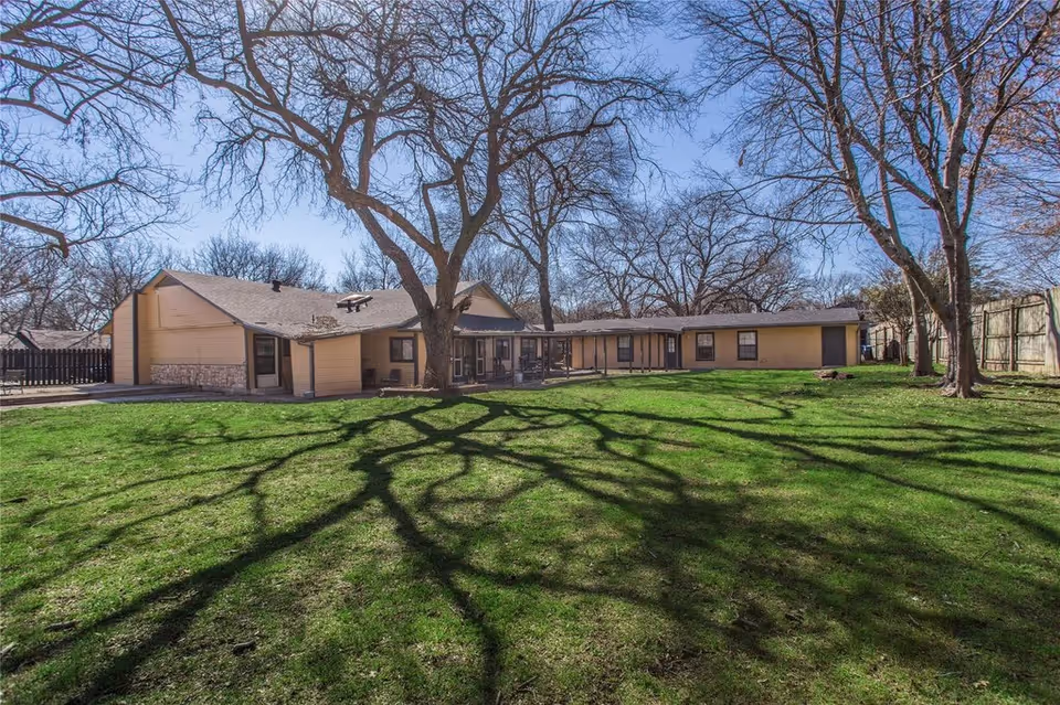 Single-story building with a large grassy yard and leafless trees casting shadows across the lawn.