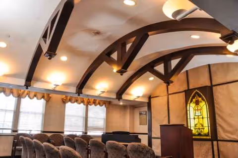 Interior of a senior living facility chapel with stained glass, wooden beams, and chairs.