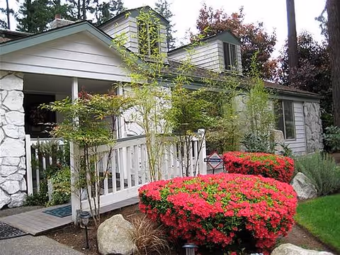 Front exterior of a home-style senior living residence with stone accents, porch, and vibrant landscaping.