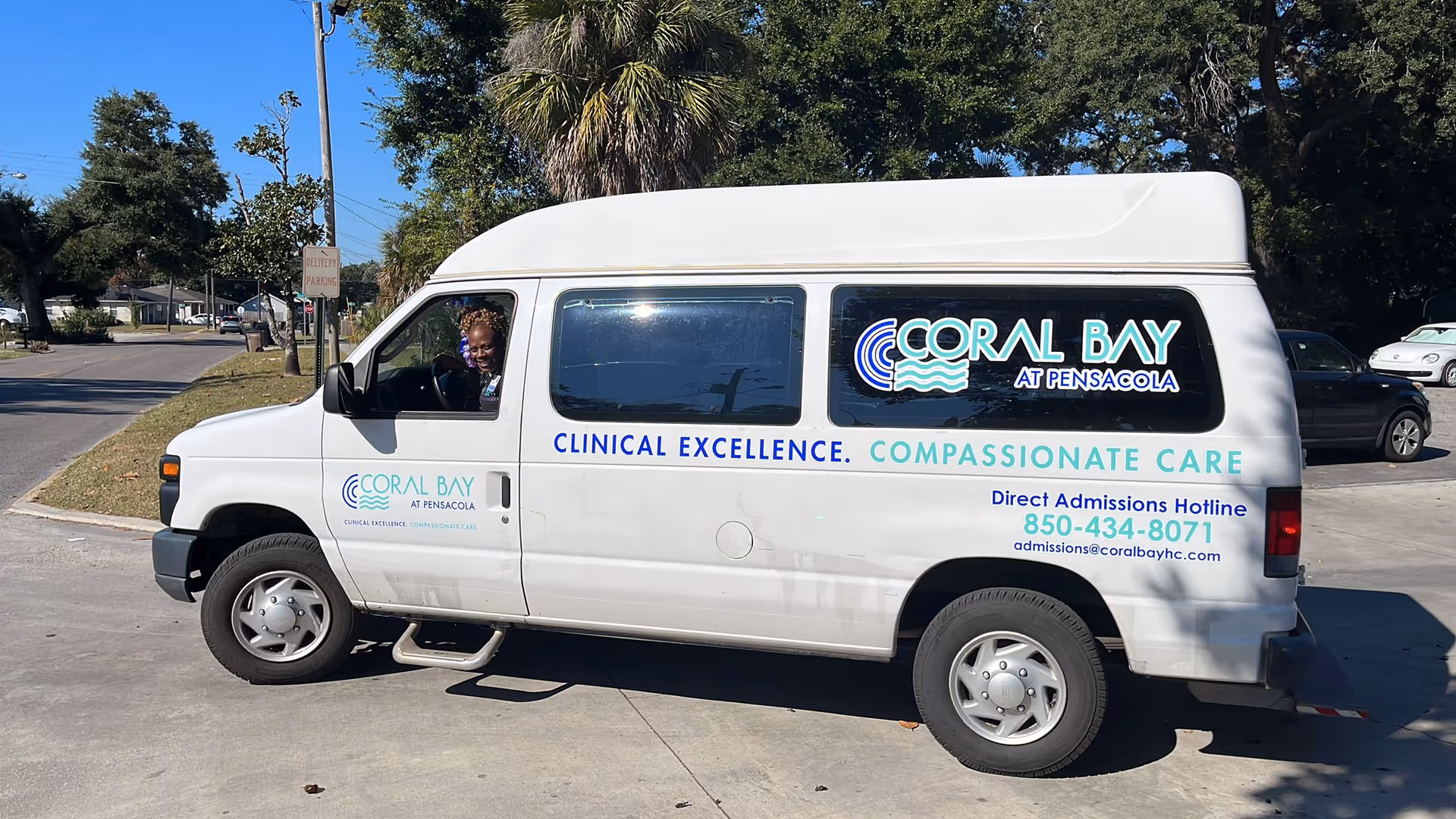 A white Coral Bay at Pensacola shuttle van parked outside with branded signage and a driver visible in the front seat.