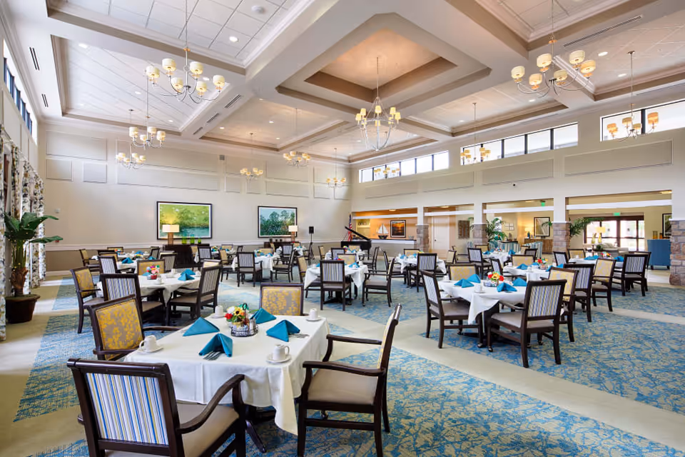 Spacious, well-lit dining room with multiple tables set with white linens and teal napkins under chandeliers.
