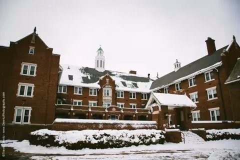 Brick senior living facility exterior in snow with a covered entrance and steps.
