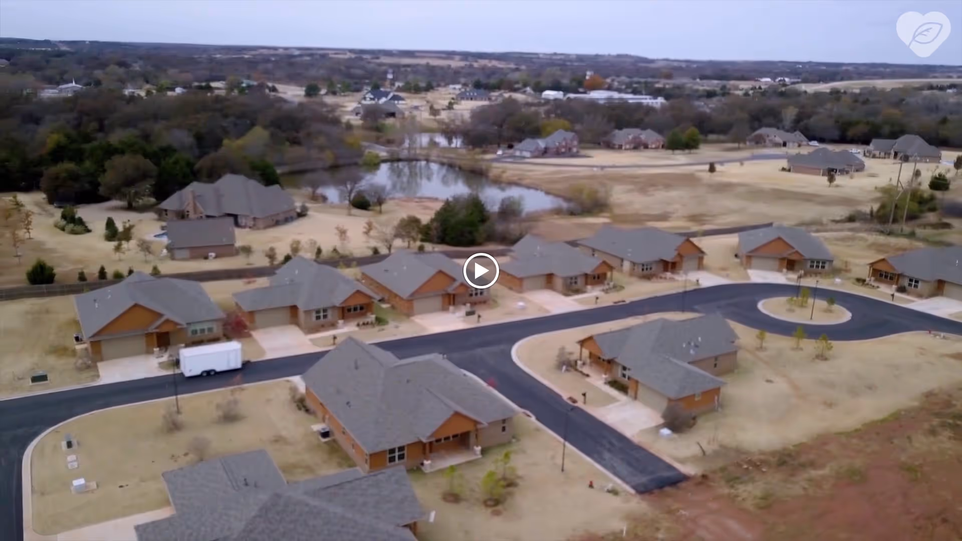 Aerial view of single-story ranch-style homes arranged along curving roads with a pond and open landscape in the background.