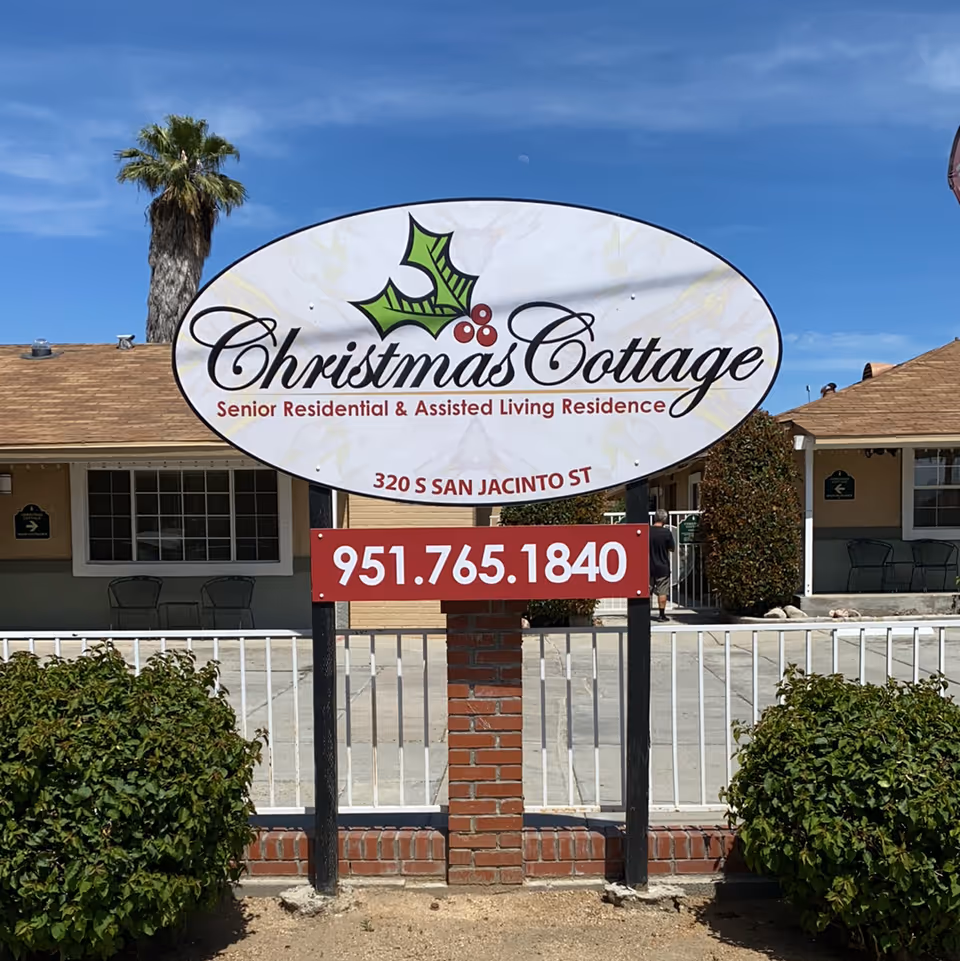 Entrance sign reading 'Christmas Cottage Senior Residential & Assisted Living Residence' with a phone number mounted on a brick post in front of a single-story building.