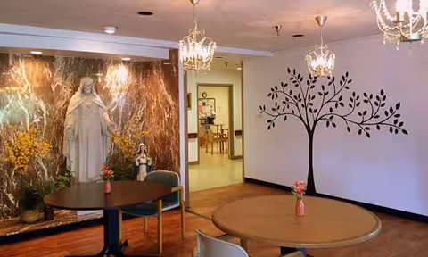 Interior dining area at Vincentian De Marillac with round tables, chandeliers, statues, and wall mural.