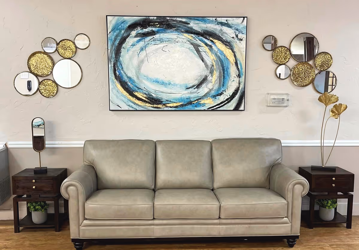 Beige leather sofa in a sitting area with abstract wall art, circular mirrors, and two side tables with decorative items.
