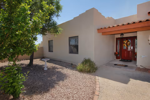 Exterior view of a single-story senior living building with a red front door and gravel yard.