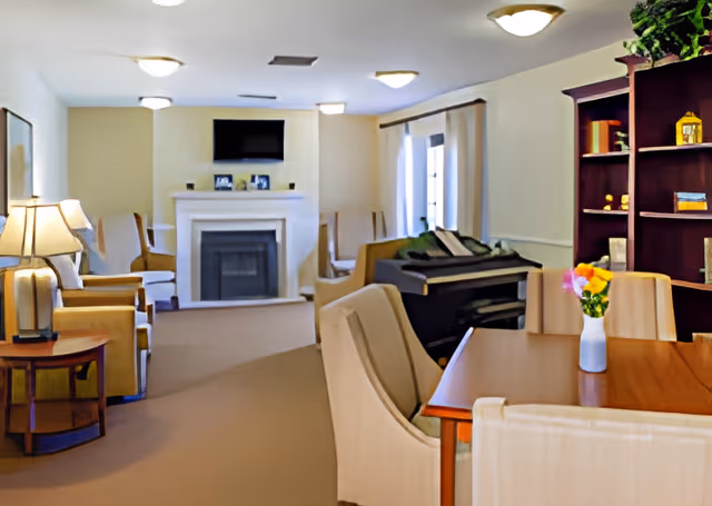 Bright communal living room with seating, a fireplace and TV, a piano, dining table, and bookshelf.