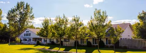 Front view of Encore Assisted Living and Memory Care at Hugo, with trees and a lawn.