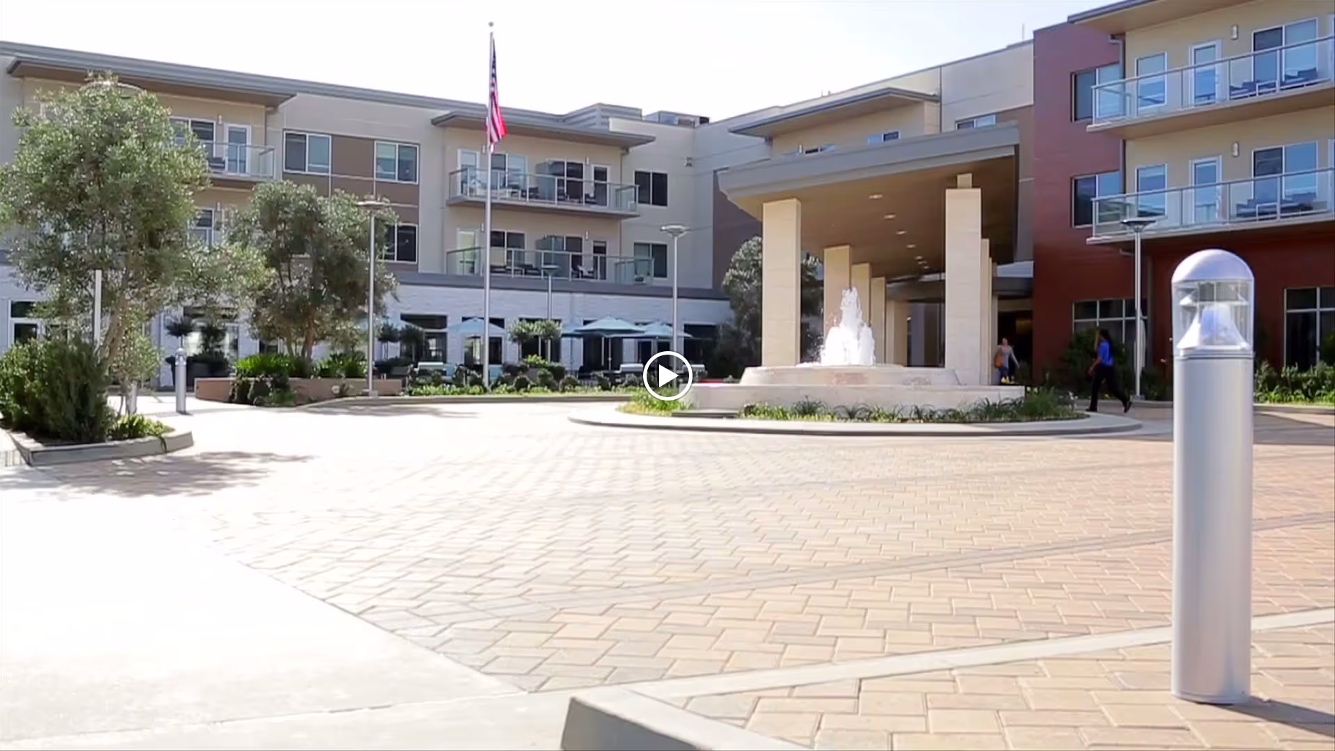 Front entrance courtyard of a multi-story residential building with a central fountain, flagpole, and covered porte-cochère.