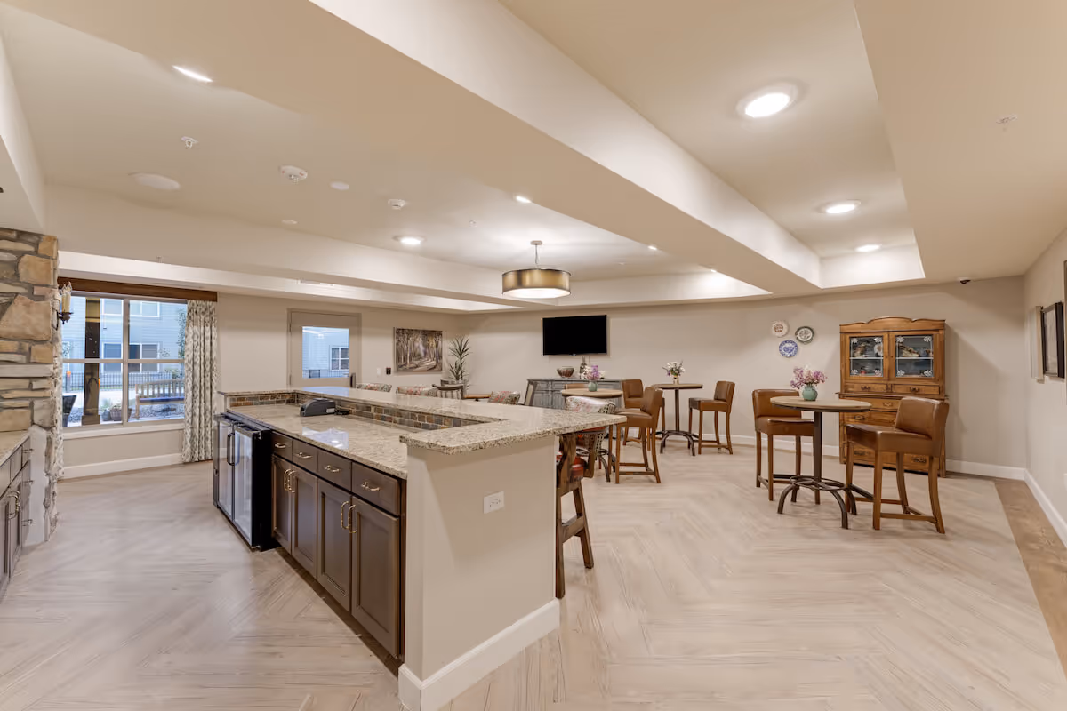 Open communal dining area and kitchenette with a granite island, high-top tables and chairs, and a wall-mounted TV.