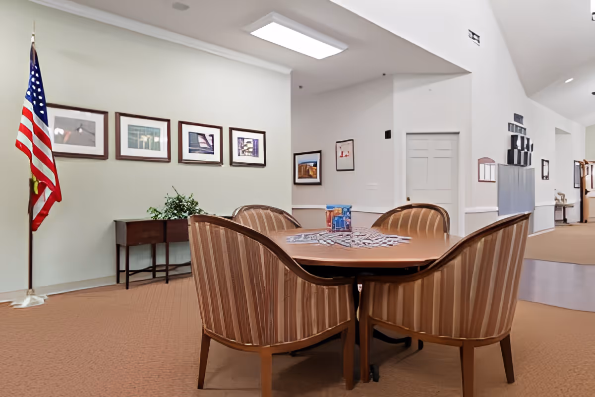Round table with striped upholstered chairs in a communal interior room decorated with framed art and an American flag.