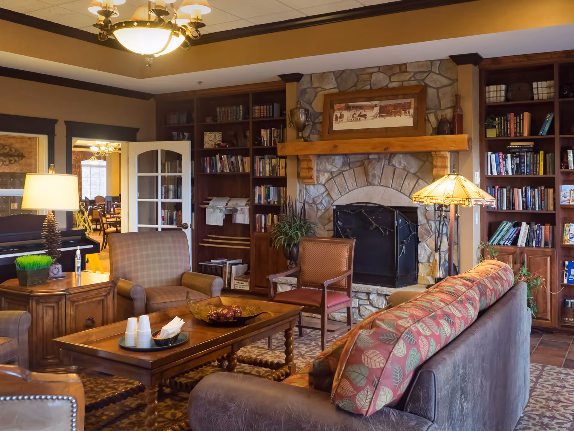 Cozy living room with a stone fireplace, built-in bookshelves, sofas and armchairs arranged around a wooden coffee table.