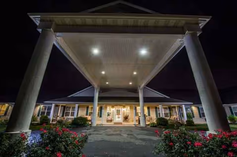Night view of Amity Place entrance with illuminated columns and flowers.