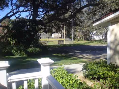 Front view of a senior living facility showing a porch, shrubs, and tall trees.
