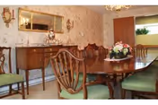 Formal dining room with a long wooden table, upholstered chairs, a sideboard, chandelier, and floral wallpaper.