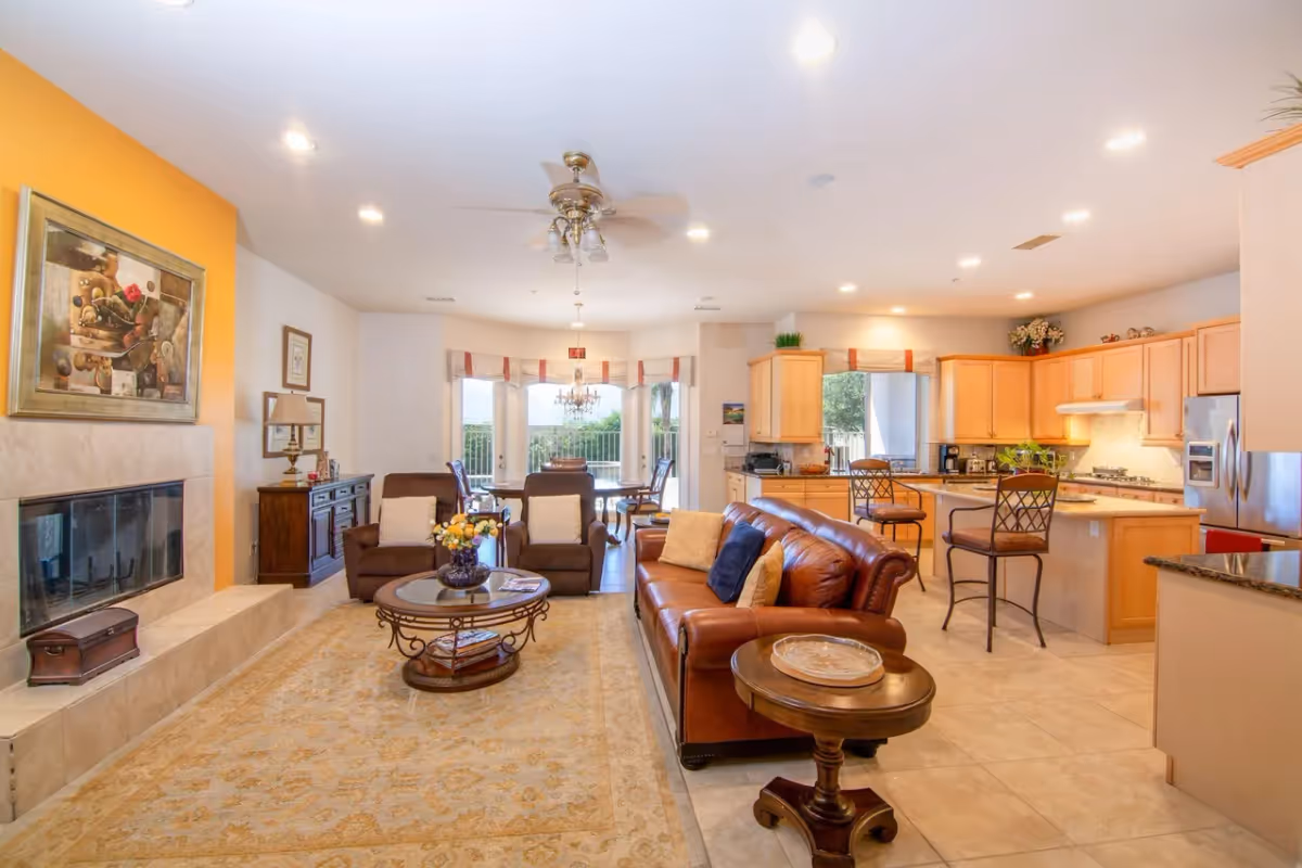 Open-plan living room and kitchen with a leather sofa, armchairs, fireplace, dining table, and a kitchen island with bar stools.