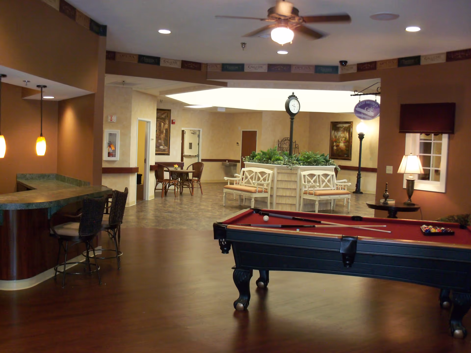 Interior common room with a pool table, bar counter, seating tables and a central planter topped with a clock.